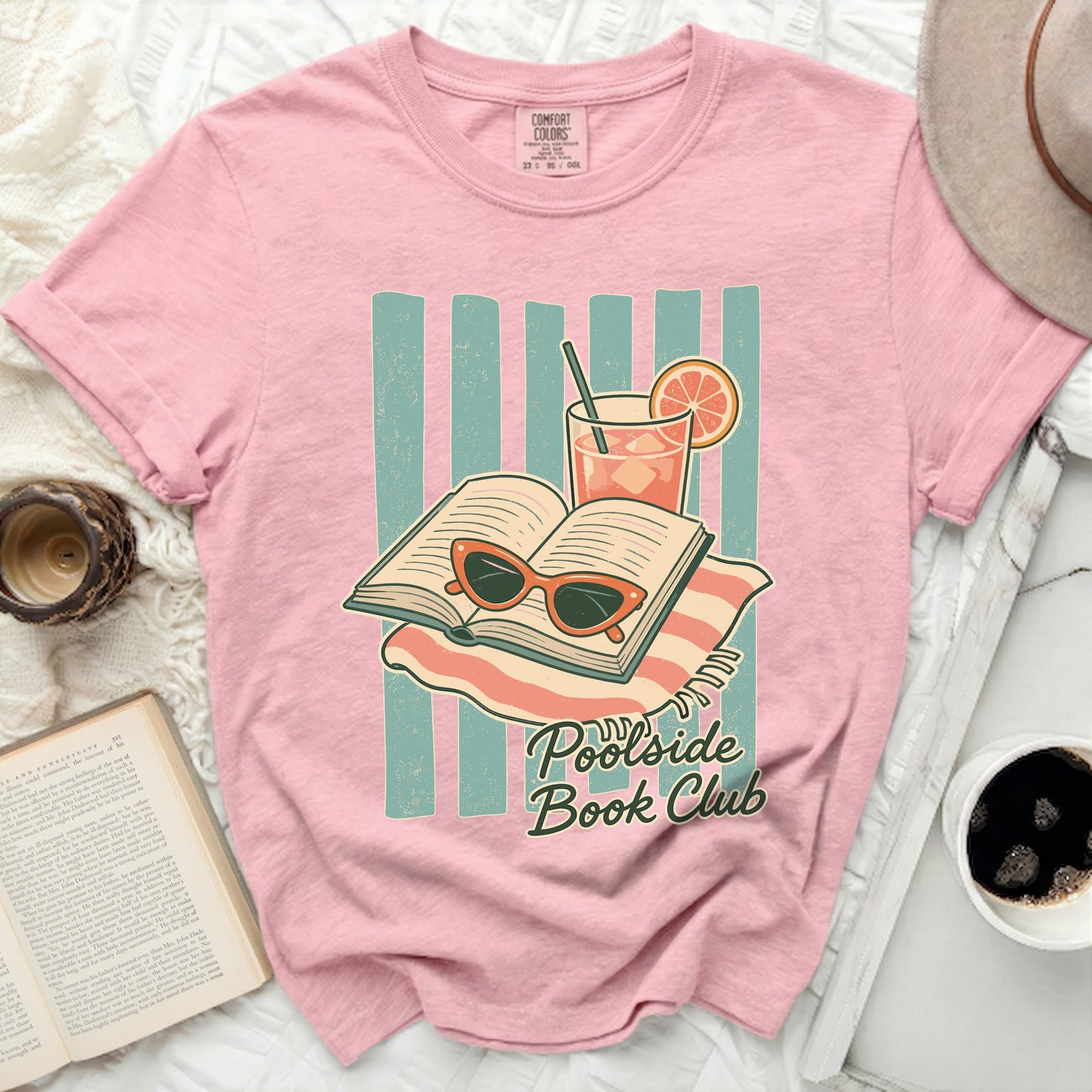 Pink t-shirt with "Poolside Book Club" text, open book, sunglasses, and drink.