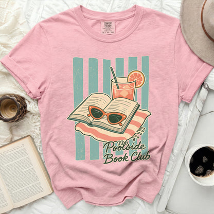 Pink t-shirt with "Poolside Book Club" text, open book, sunglasses, and drink.