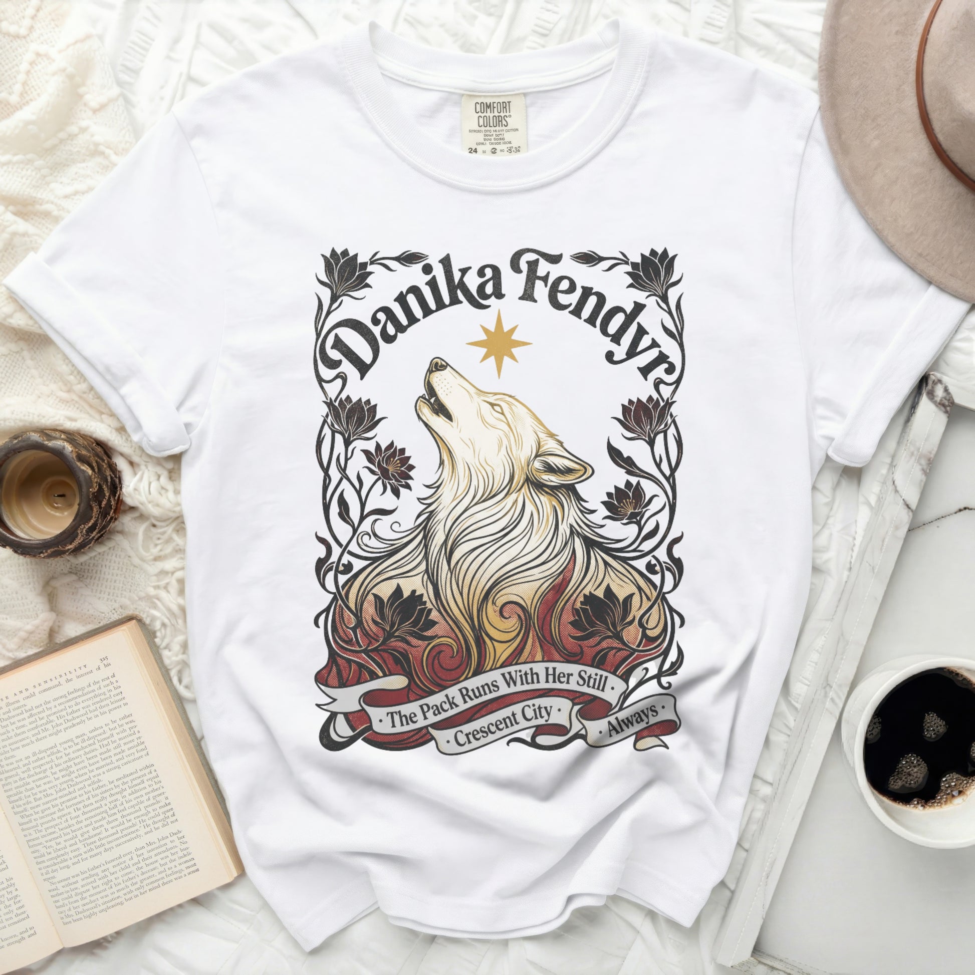 White t-shirt with wolf and floral artwork, "Danika Fendyr" and "The Pack Runs With Her Still Crescent City" text.