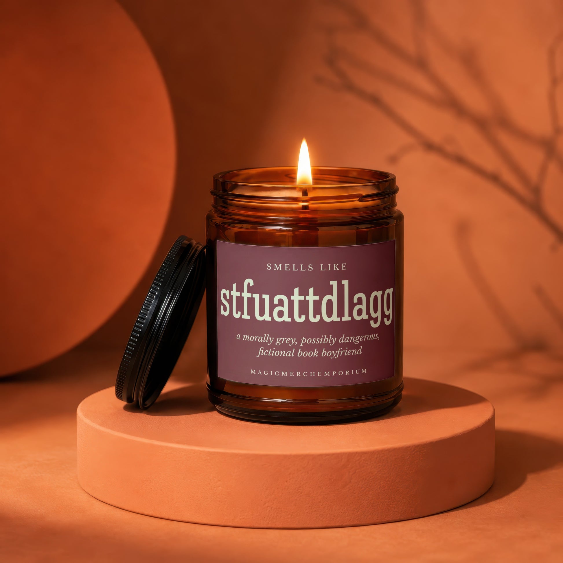 Amber jar candle with lit flame, label reads "stfuattdlaggg, a morally grey, possibly dangerous, fictional book boyfriend".