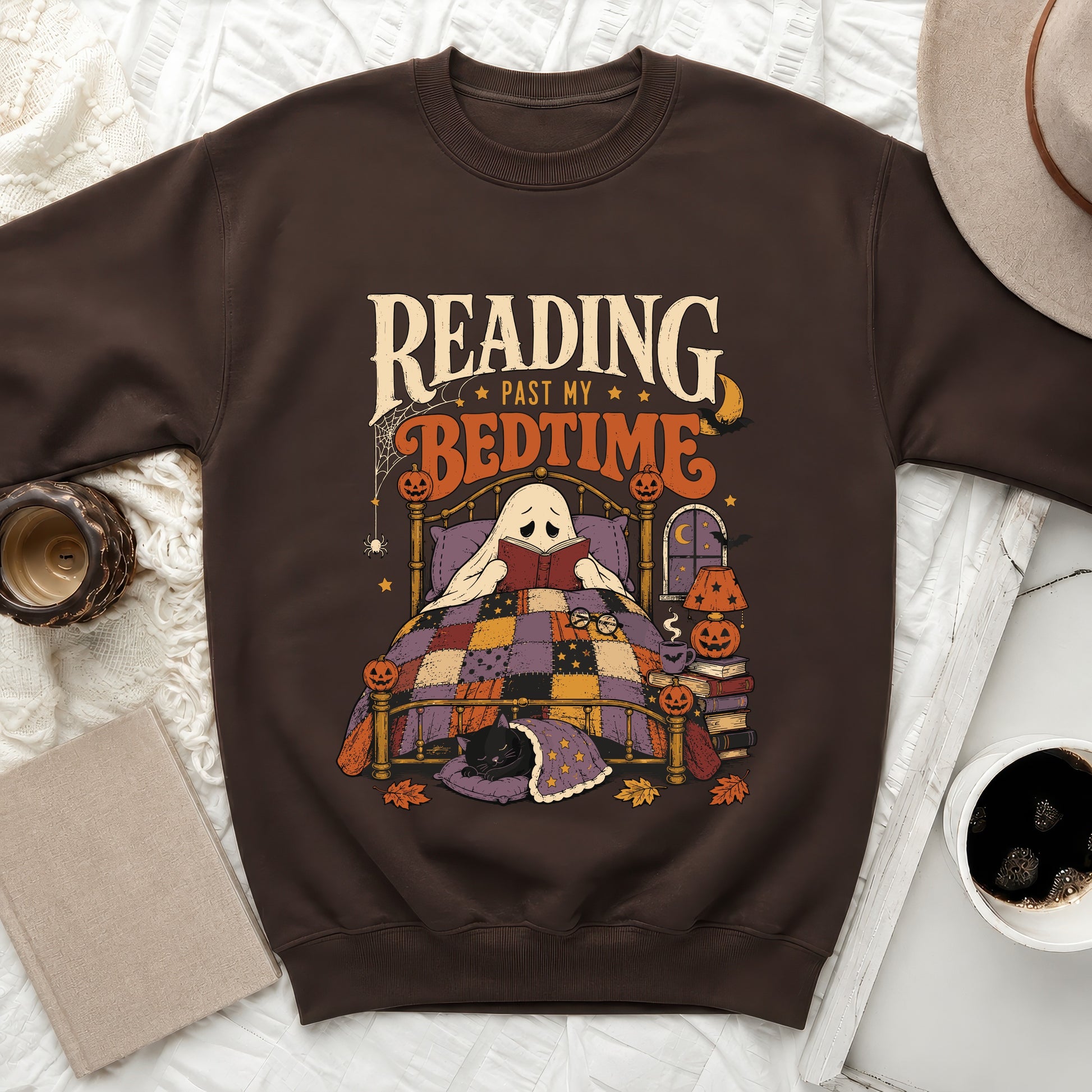 Brown sweatshirt with a ghost reading a book in bed with a sleeping cat.