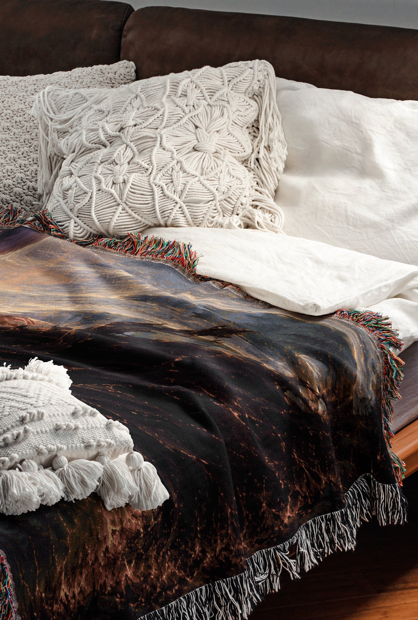 a cozy and inviting bedroom scene, featuring a bed with a dark blanket and white pillows, a brown leather couch, and a colorful throw blanket with fringe.