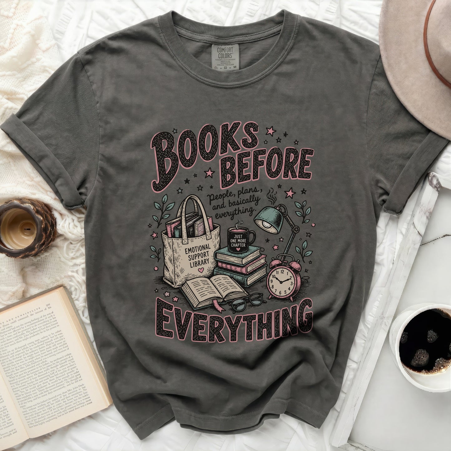 Dark grey t-shirt with "Books Before Everything" graphic and reading illustration.