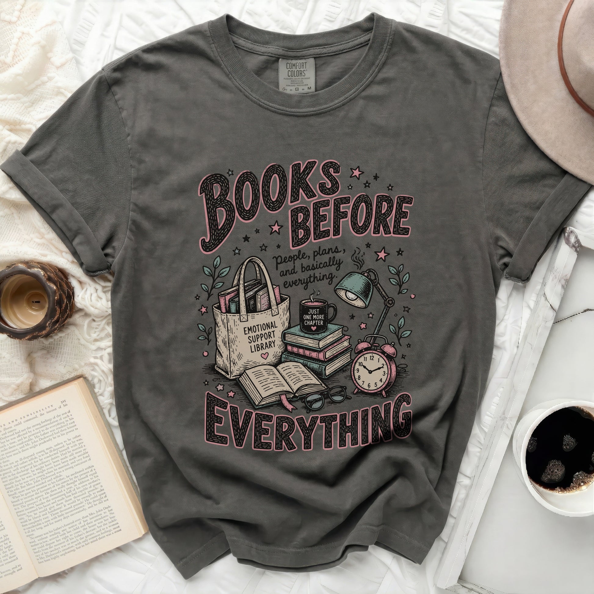 Dark grey t-shirt with "Books Before Everything" graphic and reading illustration.