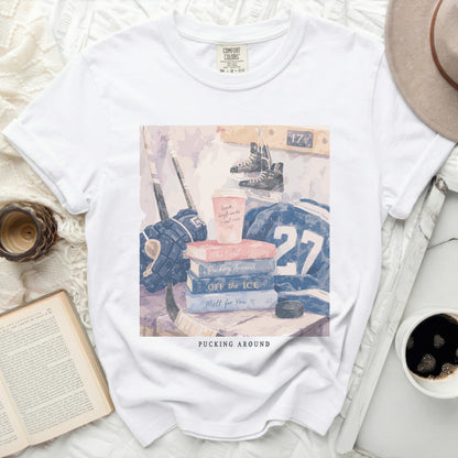 White t-shirt with "Pucking Around" text and hockey theme flat lay.