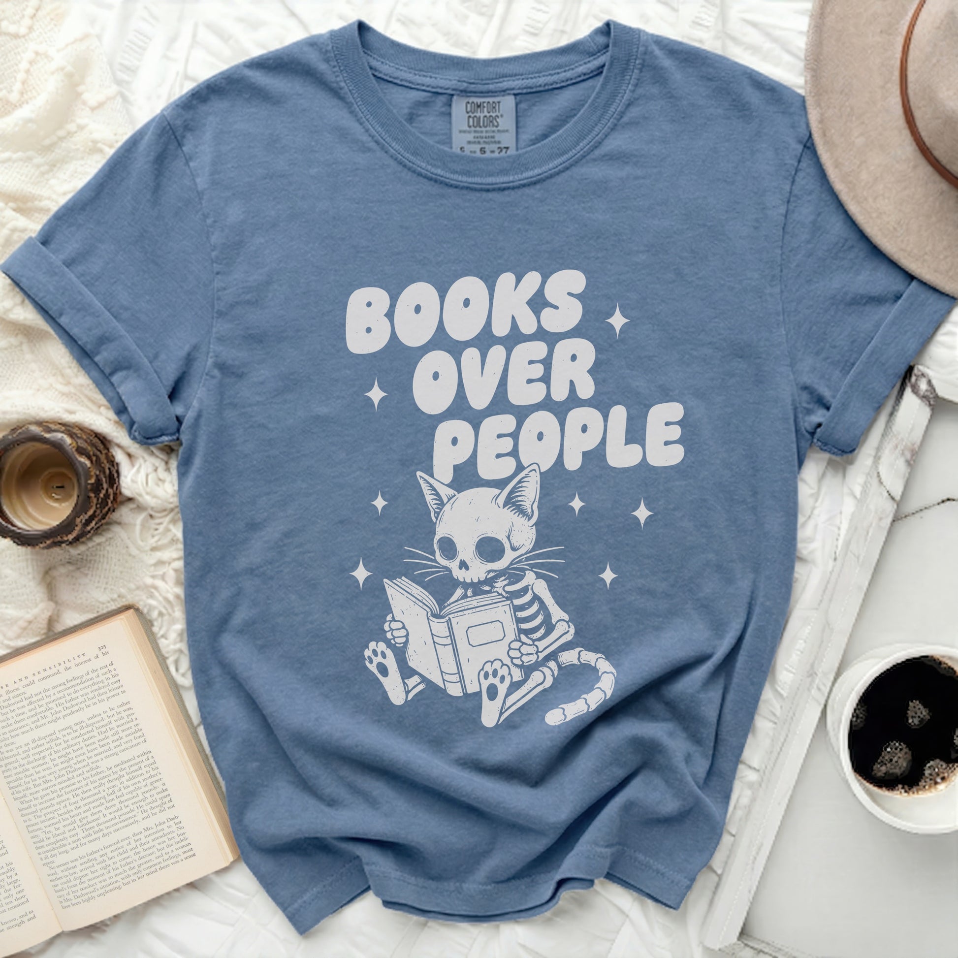 Comfort Colors blue t-shirt with white graphic of skeleton cat reading and text "BOOKS OVER PEOPLE".