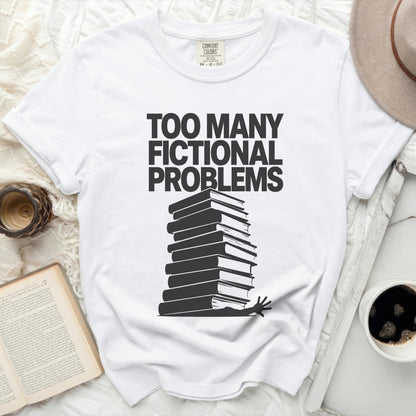 White t-shirt with "TOO MANY FICTIONAL PROBLEMS" and stack of books graphic.