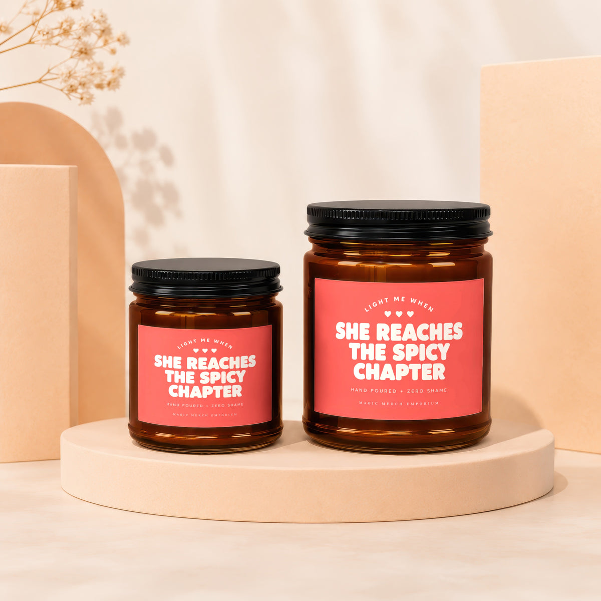 Two amber glass candles with pink labels reading "She Reaches The Spicy Chapter".