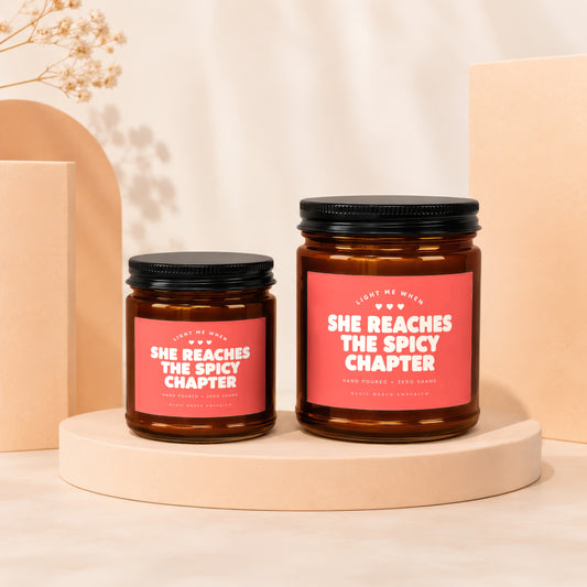 Two amber glass candles with pink labels reading "She Reaches The Spicy Chapter".