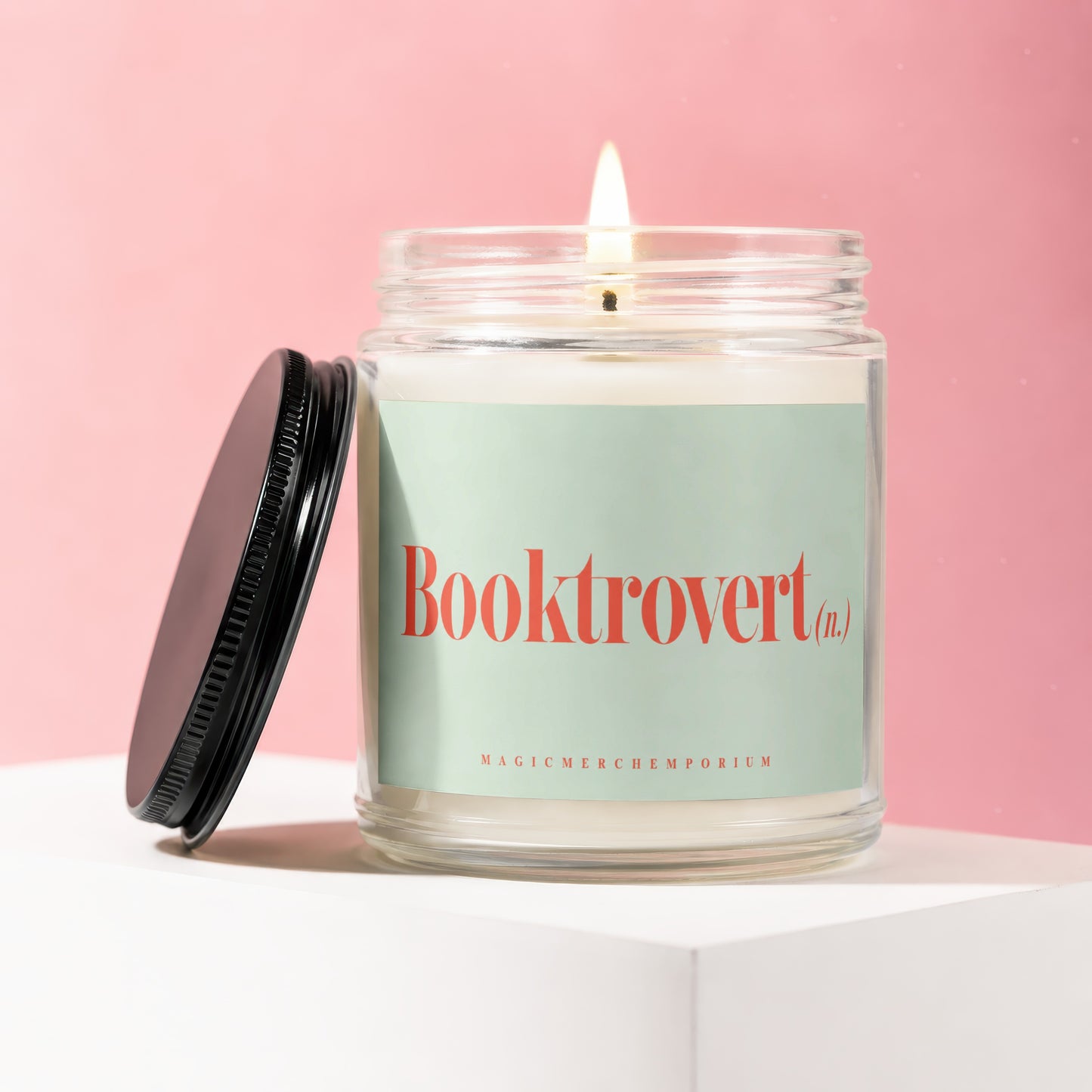 Glass candle with lit wick and "Booktrovert (n.)" on mint green label.