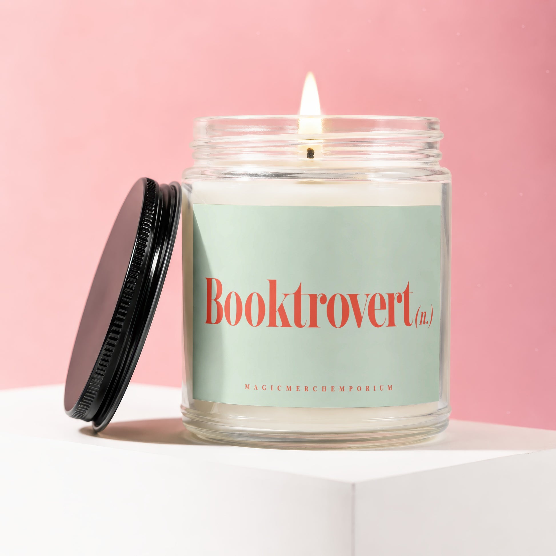 Glass candle with lit wick and "Booktrovert (n.)" on mint green label.