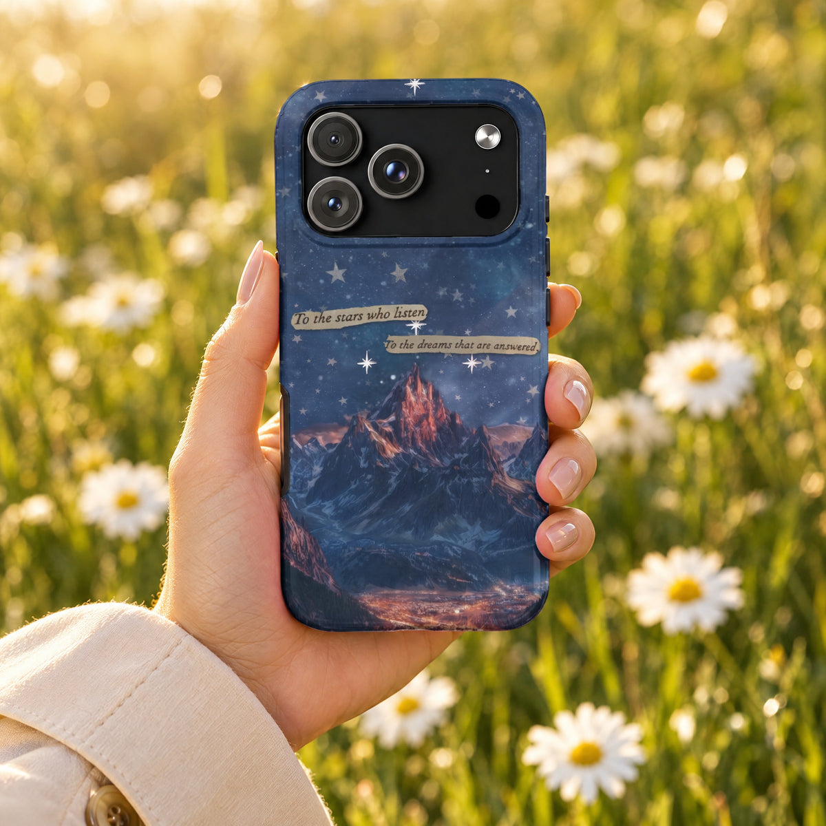 A hand holds a blue phone case featuring a mountain landscape, starry night sky, and inspirational text.