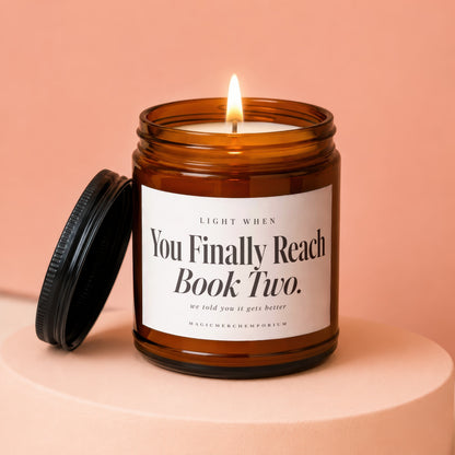 A lit candle in an amber glass jar with a black lid on a peach pedestal.