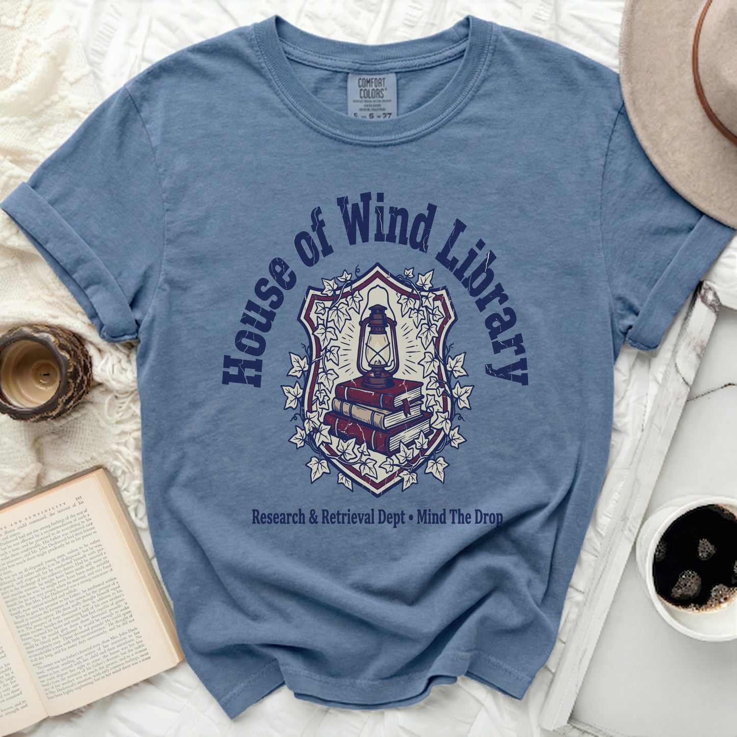 Blue t-shirt with "House of Wind Library" and a lantern over books graphic.