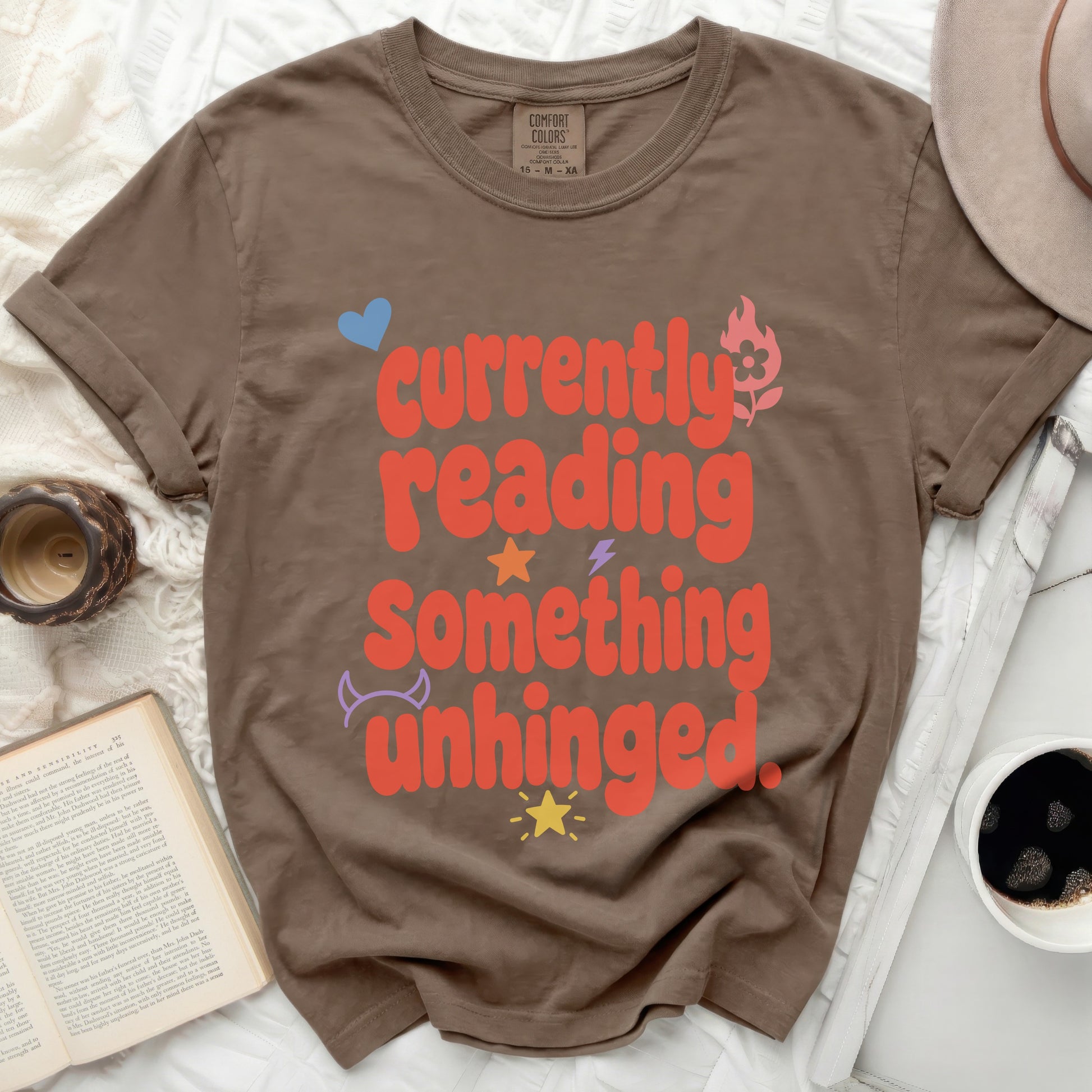 Brown t-shirt with "currently reading something unhinged" text and graphics.