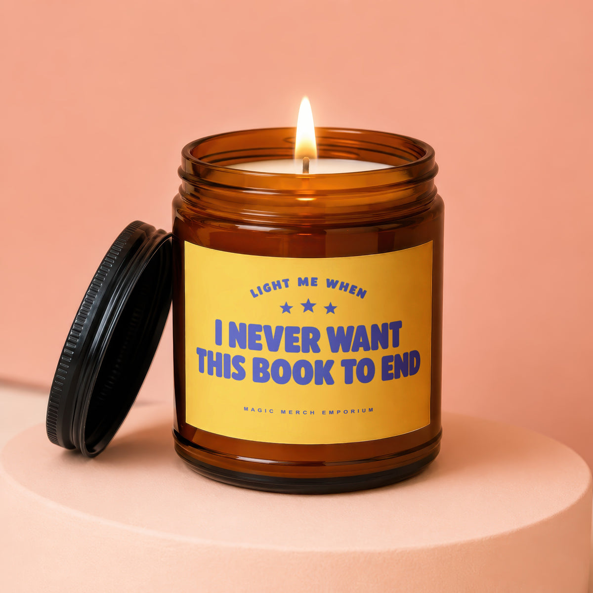 Amber candle with lid ajar, lit flame, yellow label reads "Light Me When I Never Want This Book To End".