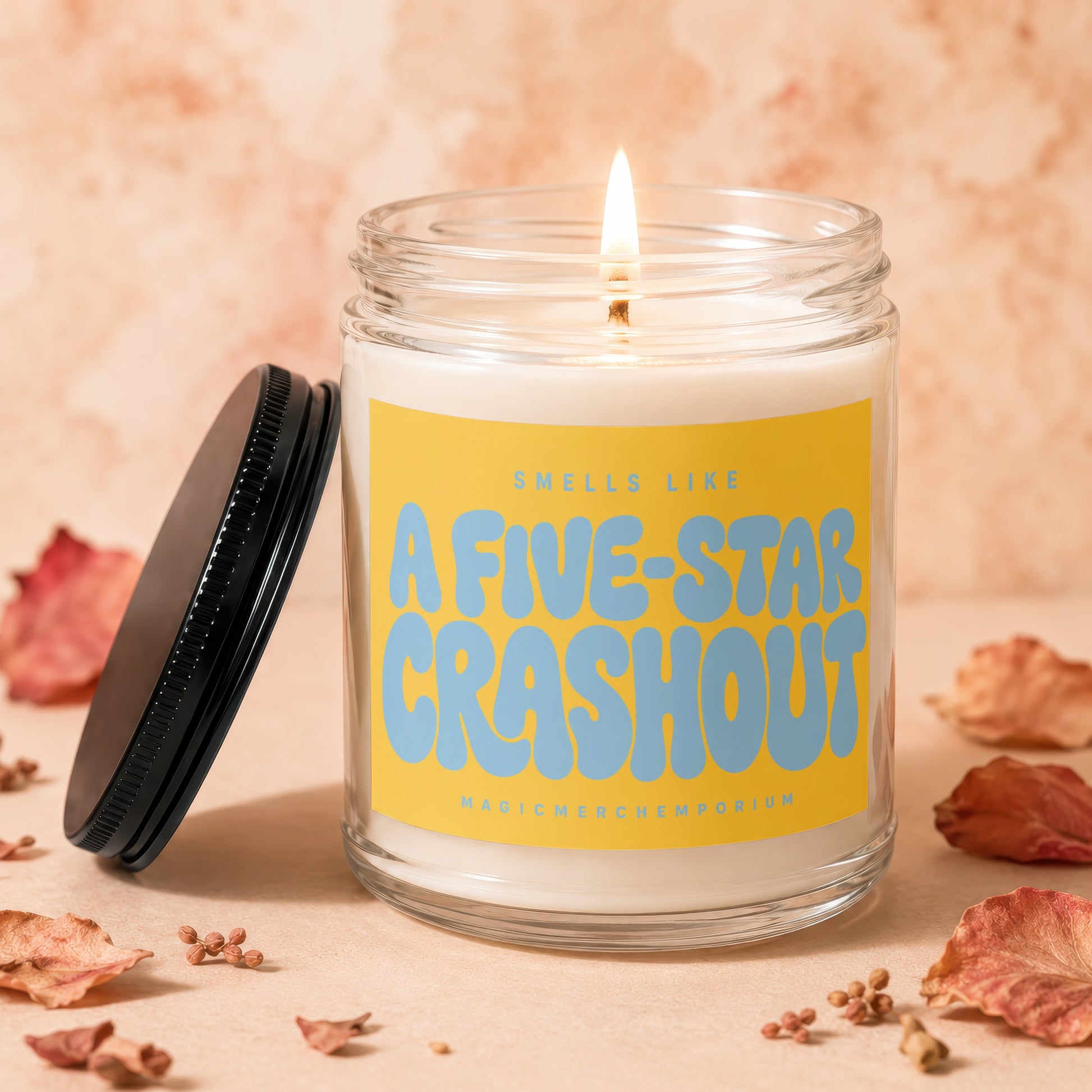 Lit candle with yellow label reading "Smells Like A Five-Star Crashout".