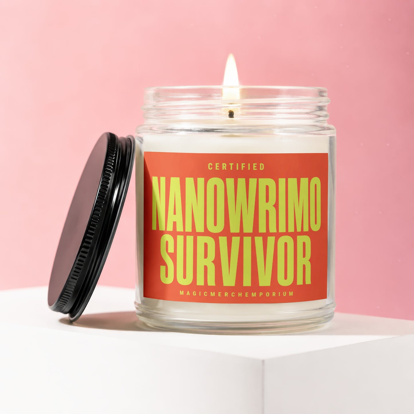 Glass candle with lit flame, black lid, and orange label reading "Certified Nanowrimo Survivor."