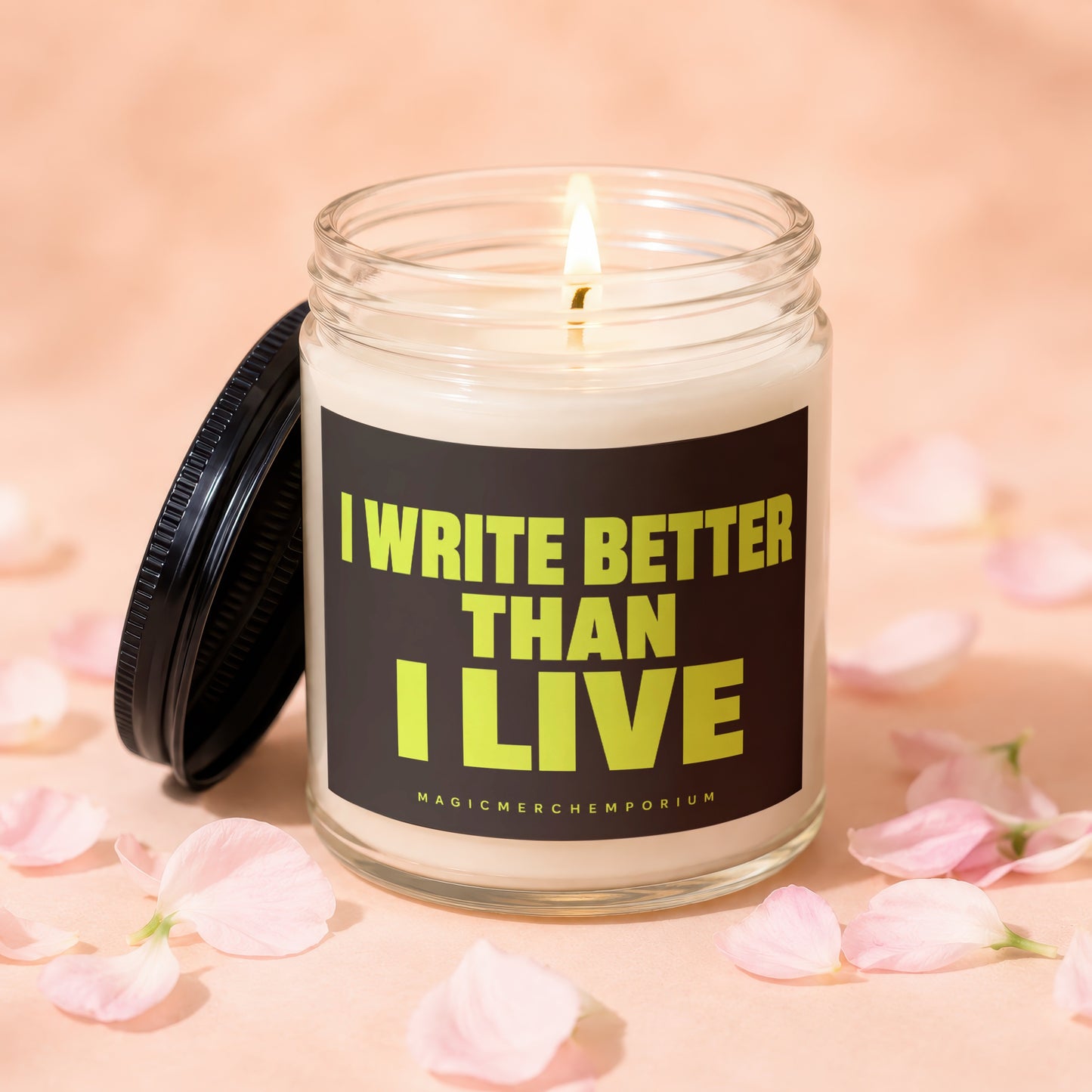 Glass candle with lit wick and black lid, featuring text "I WRITE BETTER THAN I LIVE".