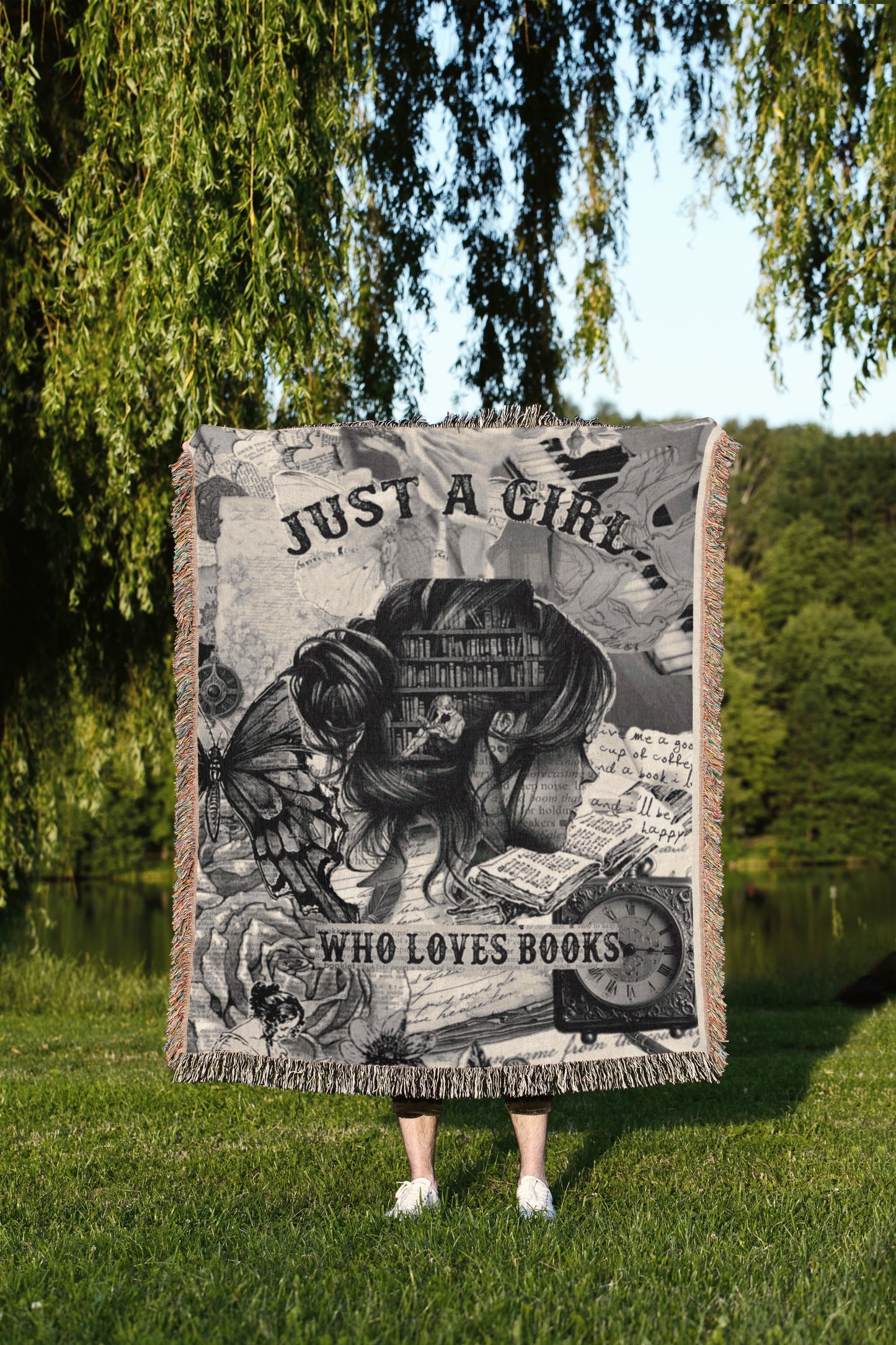 A person is standing in a grassy area, holding a large blanket that features a collage of various images, including a woman's face, a butterfly, and text.