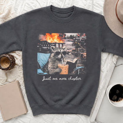 Raccoon in sunglasses drinks from a cup while reading a book with a fire in the background.