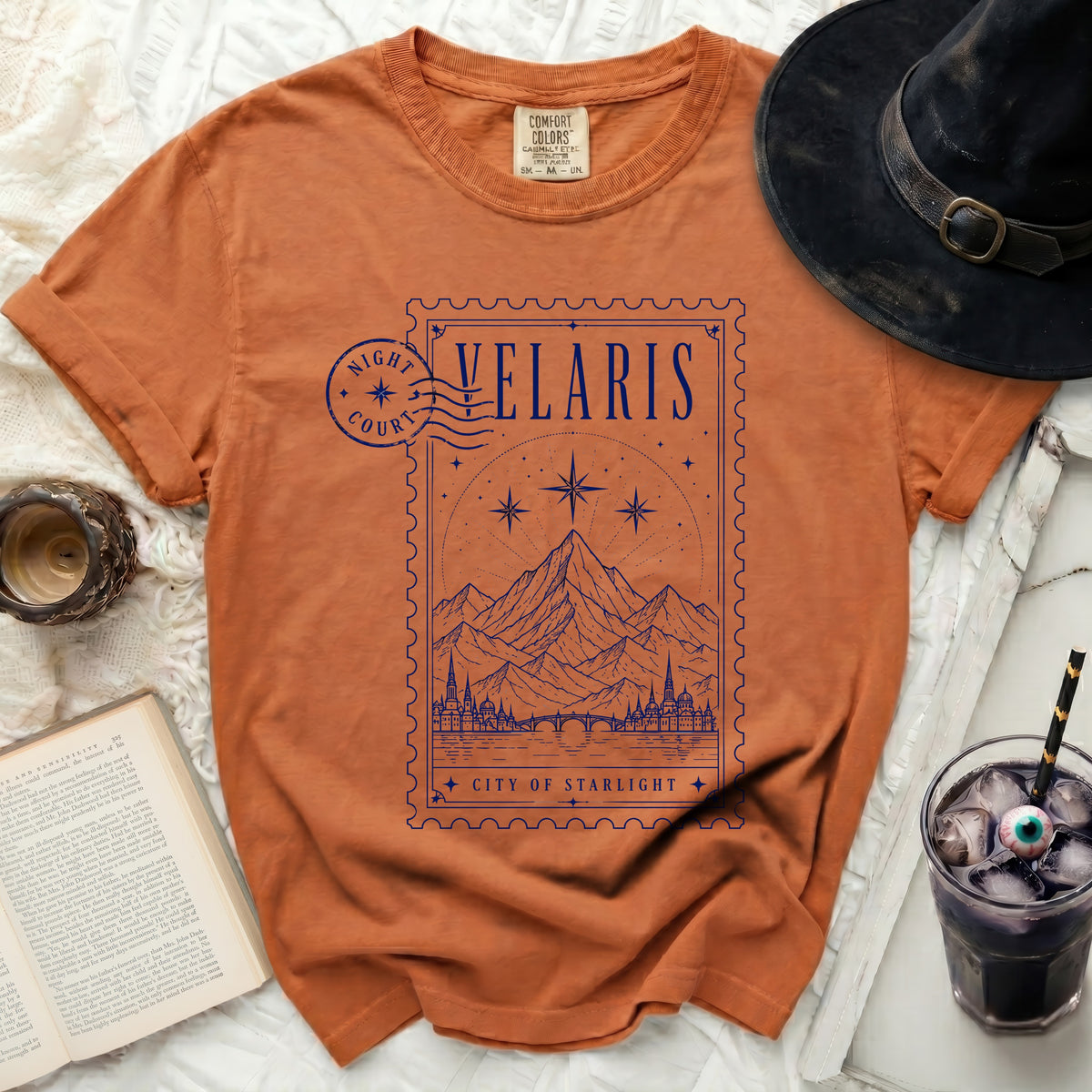 Orange t-shirt with "Velaris City of Starlight" graphic in a postage stamp design.