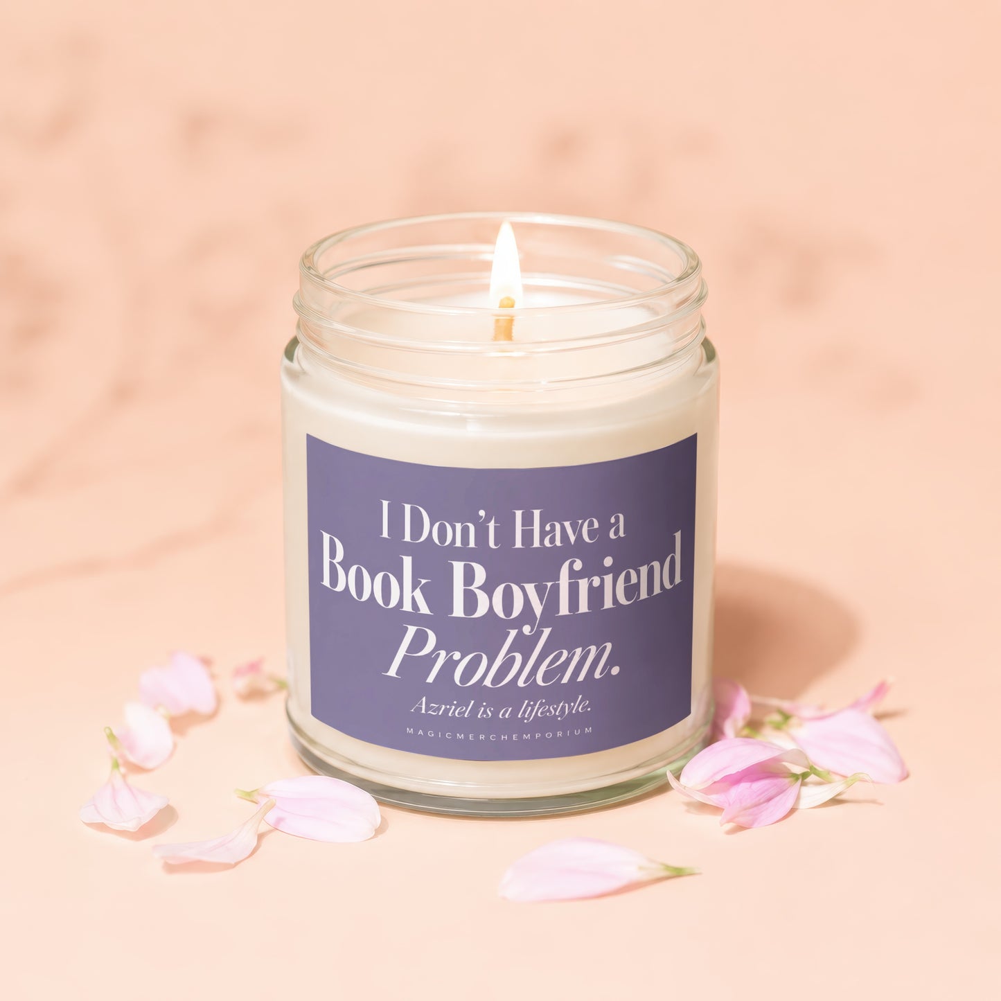 A lit candle in a glass jar with a purple label that reads "I Don't Have a Book Boyfriend Problem" surrounded by pink flower petals.
