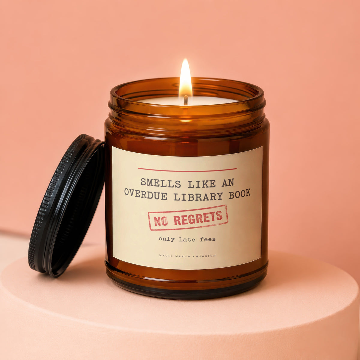 A lit candle in an amber glass jar with a label reading Smells Like an Overdue Library Book.