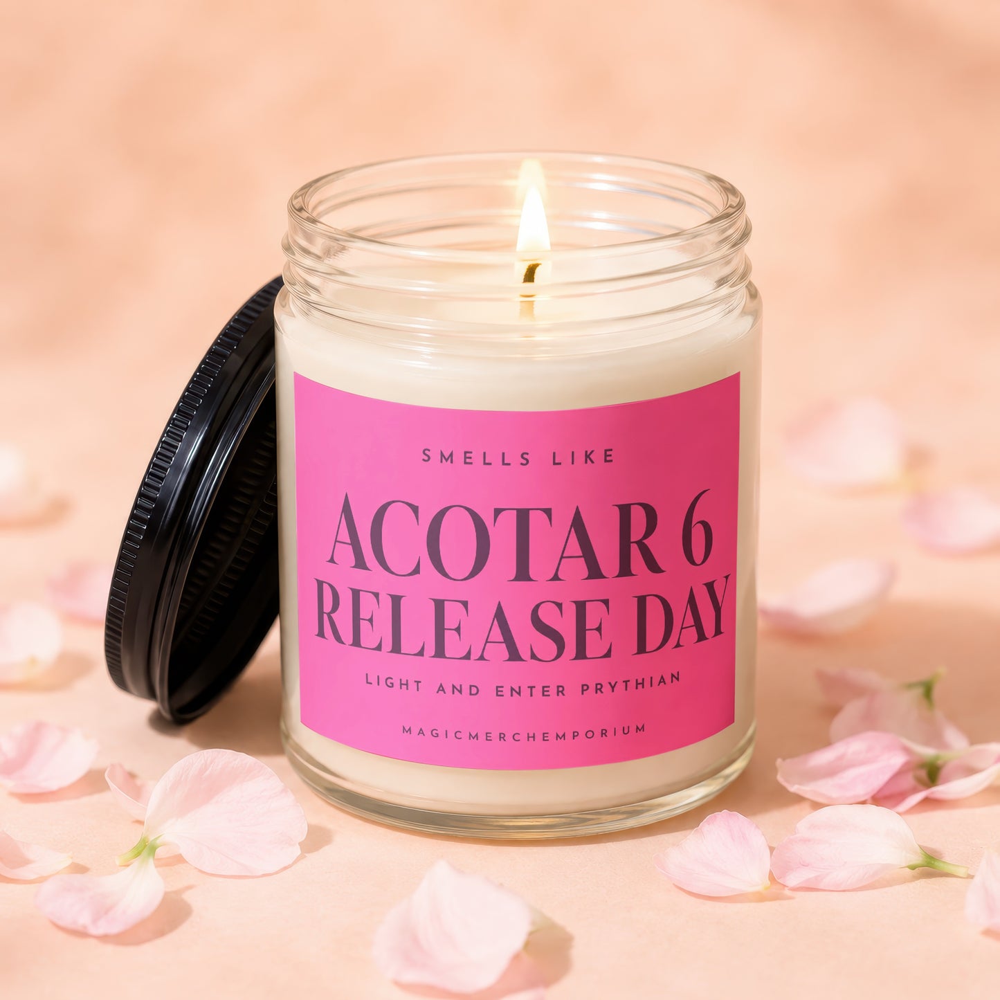 A lit candle in a glass jar with a pink label reading ACOTAR 6 RELEASE DAY, surrounded by pink petals.