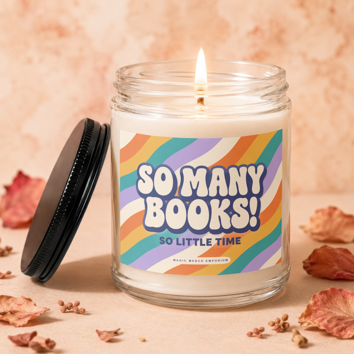 A lit candle in a glass jar with a black lid and a retro-striped label reading "So Many Books! So Little Time."
