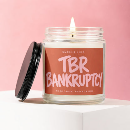 Lit candle in glass jar with black lid, label reads "Smells Like TBR Bankruptcy".