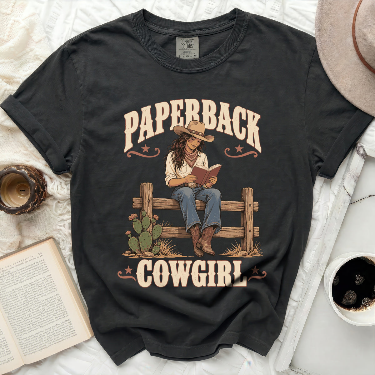 Black t-shirt graphic with "Paperback Cowgirl" text and illustration of a cowgirl reading.
