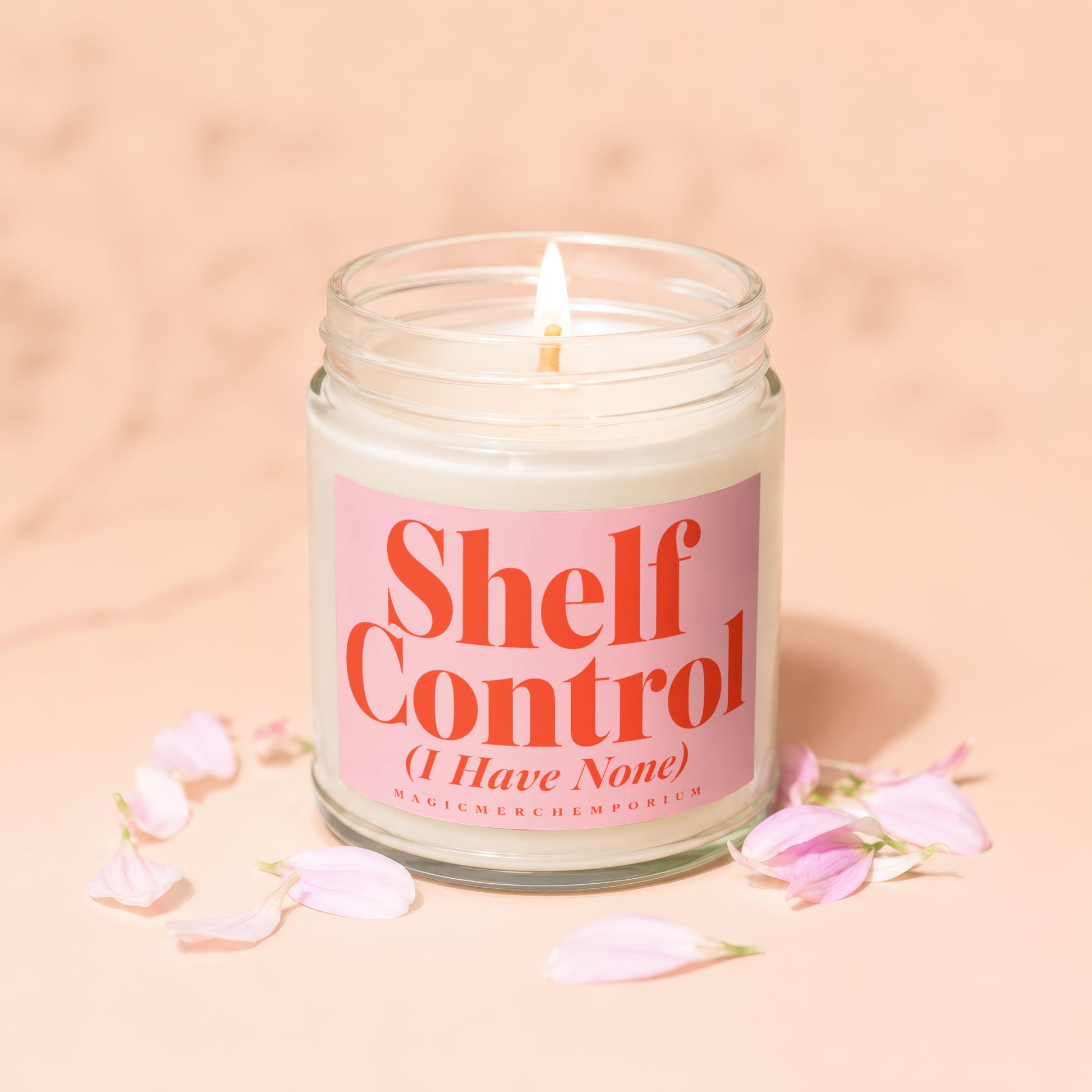 Jar candle with lit wick and pink label saying "Shelf Control (I Have None)".
