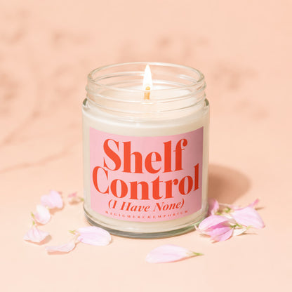 Jar candle with lit wick and pink label saying "Shelf Control (I Have None)".