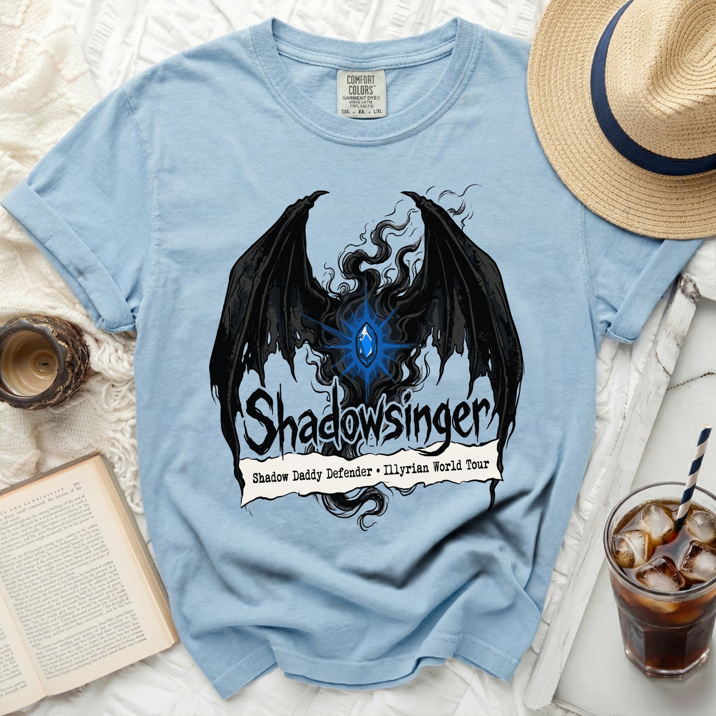Light blue t-shirt with black wings, blue gem, and "Shadowsinger" text.