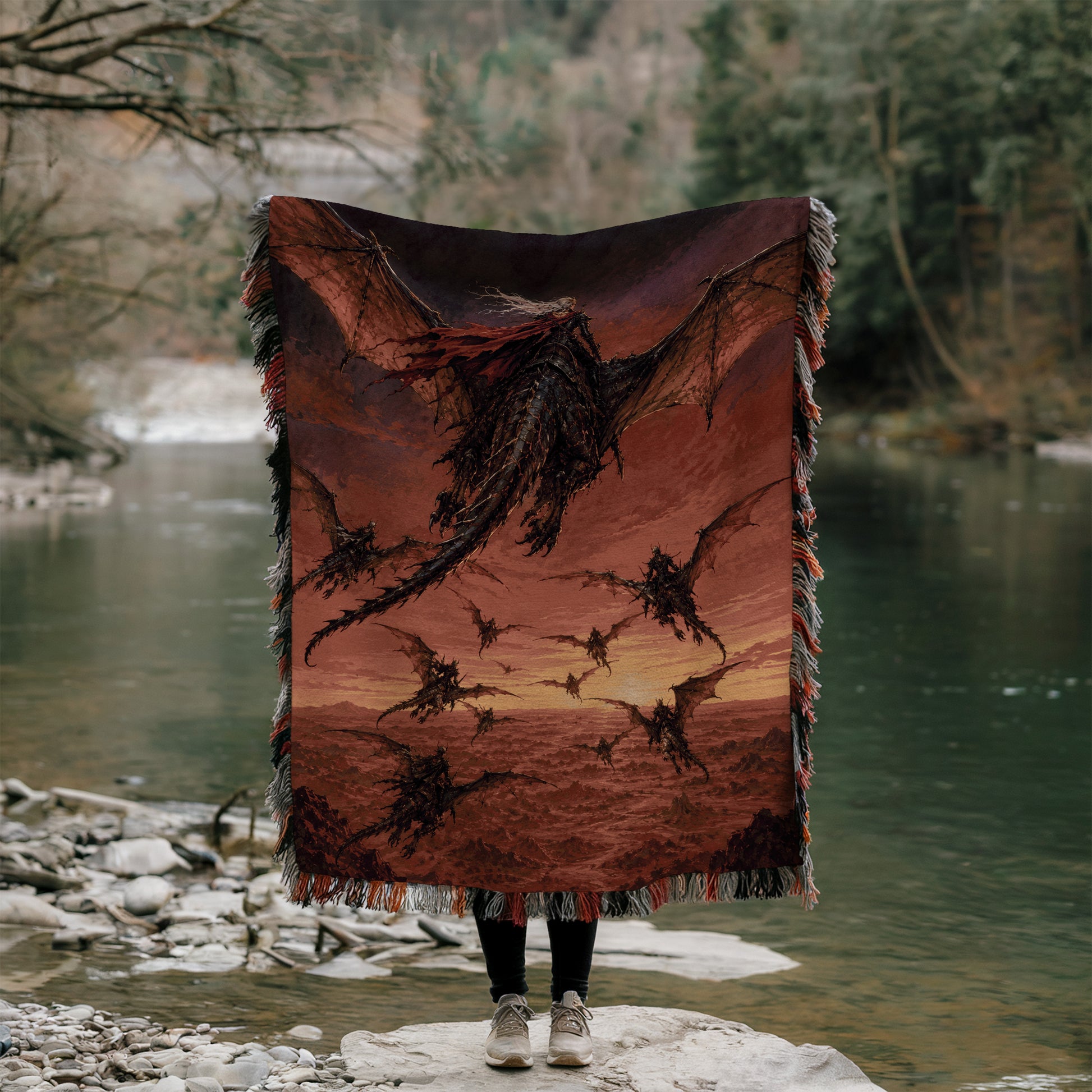 A person is standing on a rock, holding a large blanket with a dragon design on it, in front of a body of water.