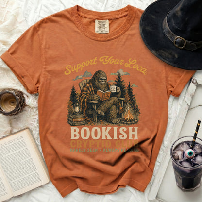 Bigfoot reading a book on a t-shirt, "Bookish Cryptid Club" text.
