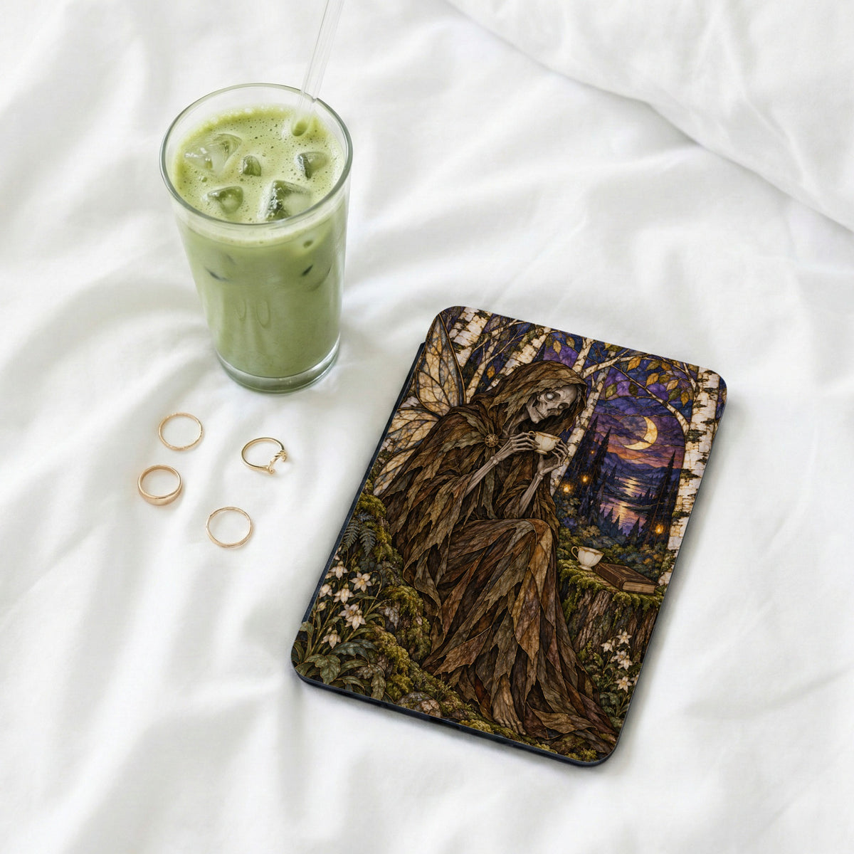 Eerie fairy illustration on a dark cover with a glass of matcha and gold rings.