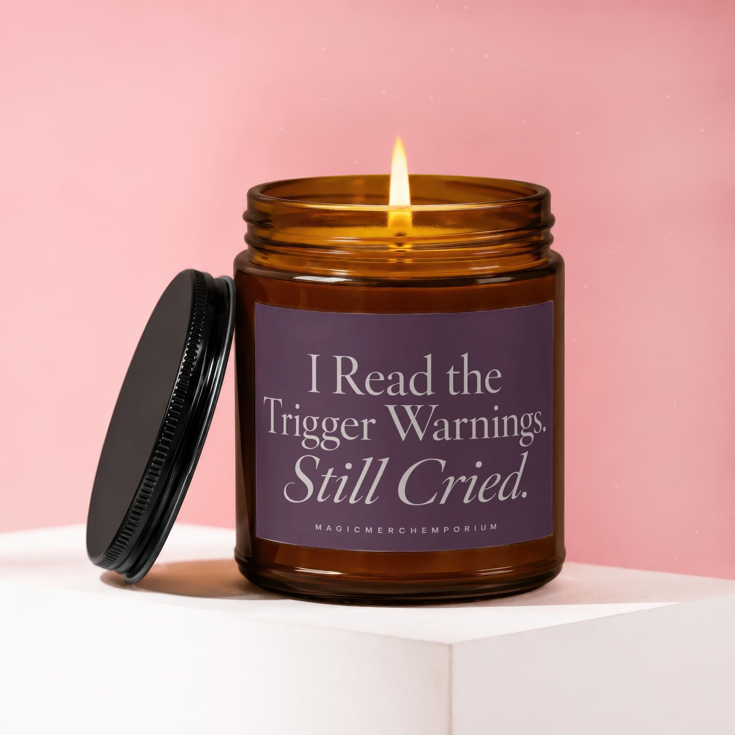 Amber glass candle with lit wick and purple label reading "I Read the Trigger Warnings. Still Cried."