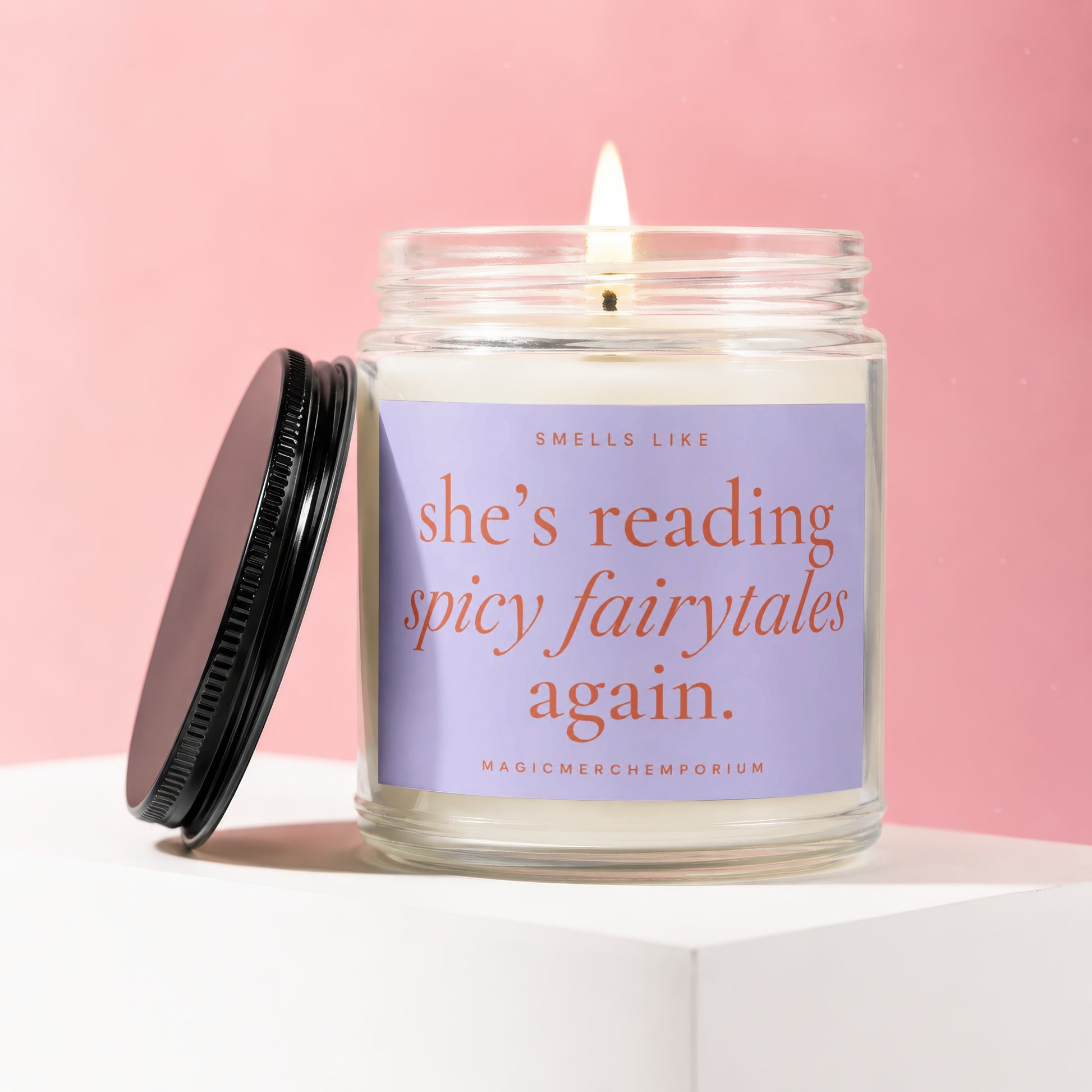 Jar candle with lit wick and black lid, labeled "Smells like she's reading spicy fairytales again."