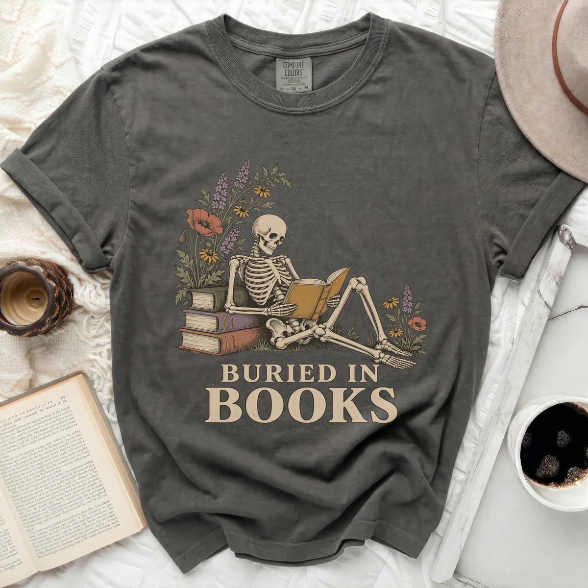 Skeleton reading a book surrounded by flowers and books, text "Buried in Books".