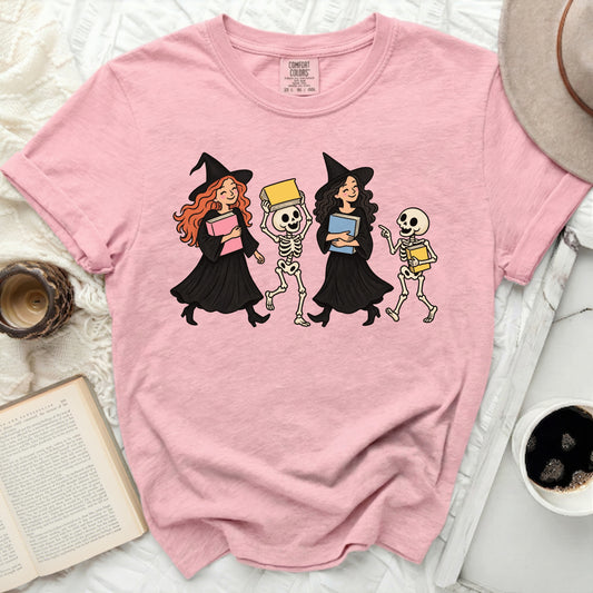 Pink t-shirt with cartoon witches and skeletons holding books.