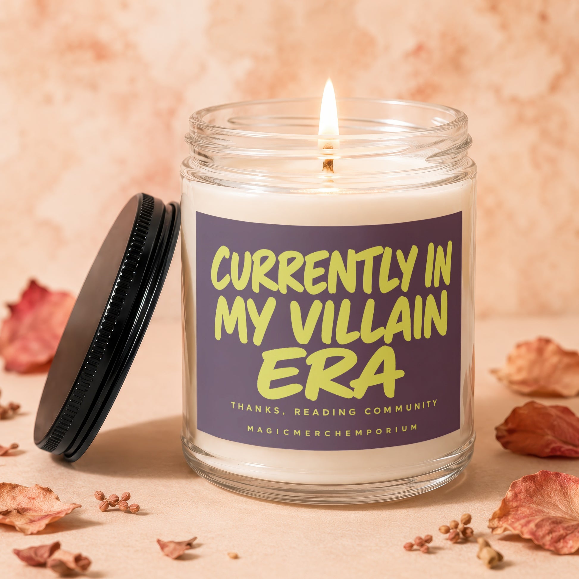 Lit candle in glass jar with label "Currently in my Villain Era" surrounded by dried leaves.