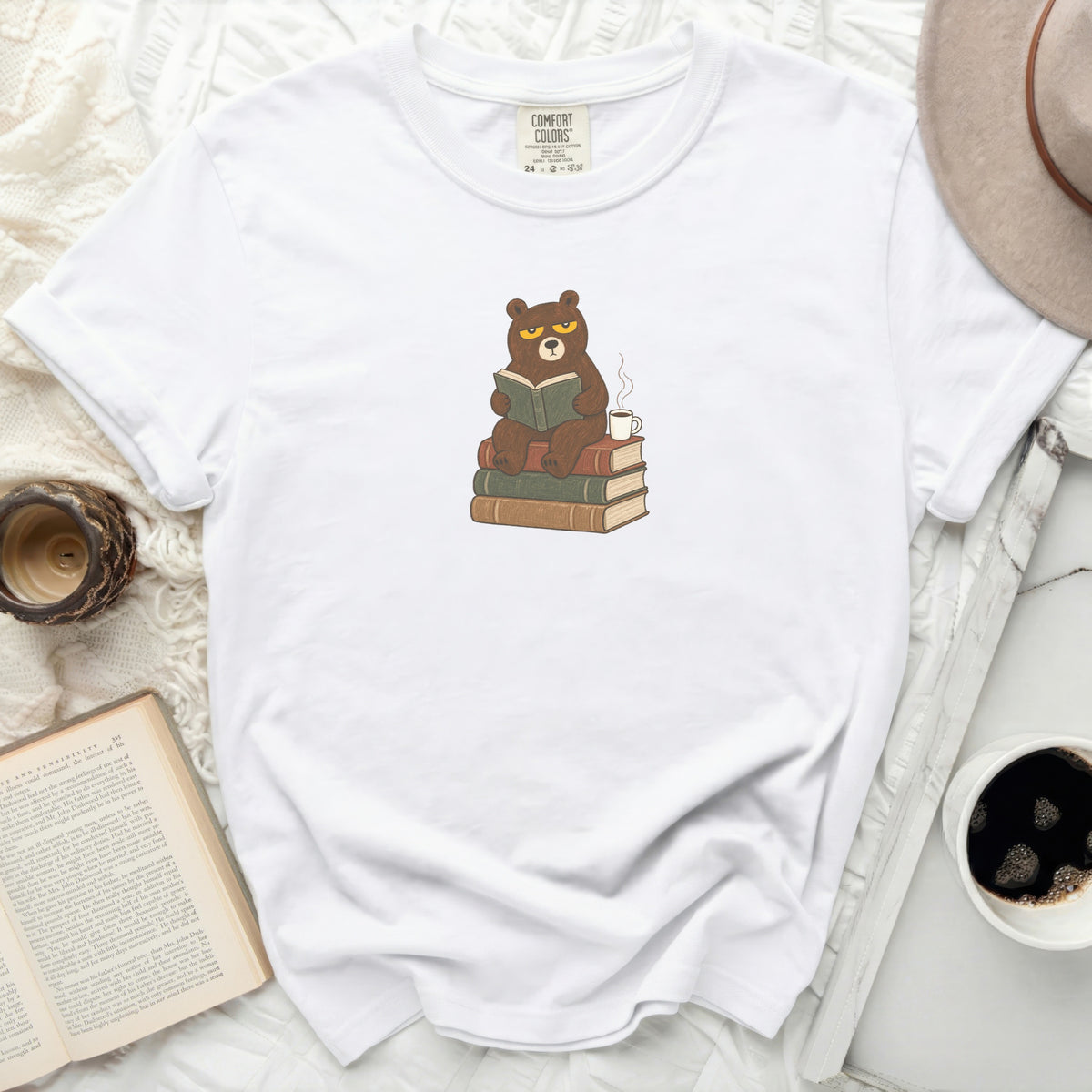 White t-shirt with a grumpy bear reading a book, sitting on books, with a coffee cup.