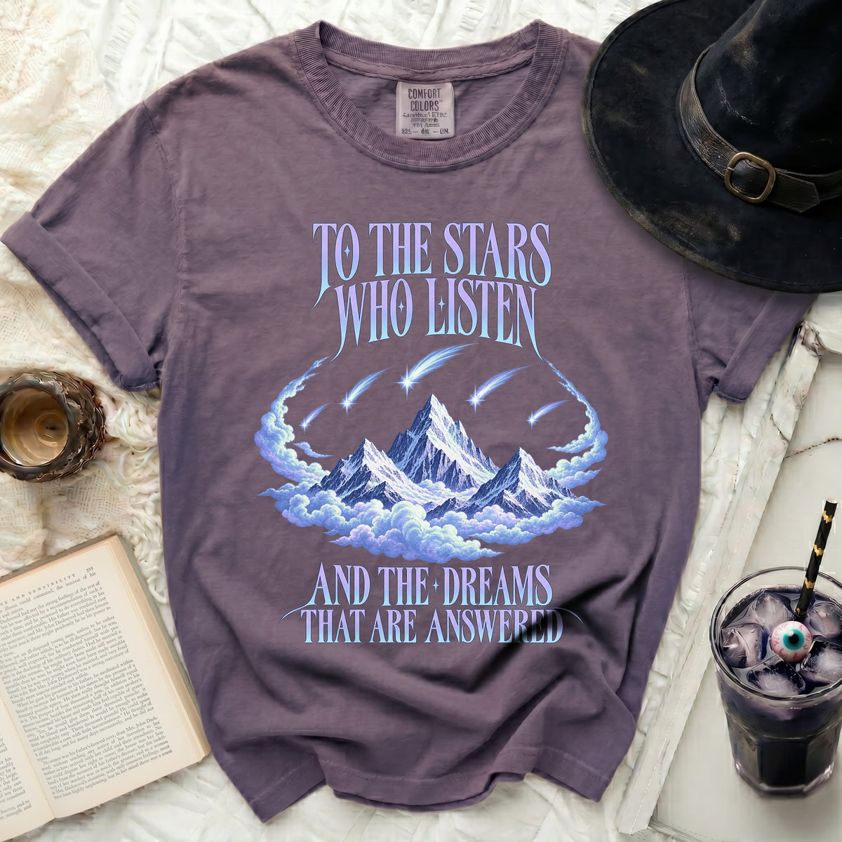 Purple t-shirt with mountains, clouds, shooting stars, and text: "TO THE STARS WHO LISTEN AND THE DREAMS THAT ARE ANSWERED."