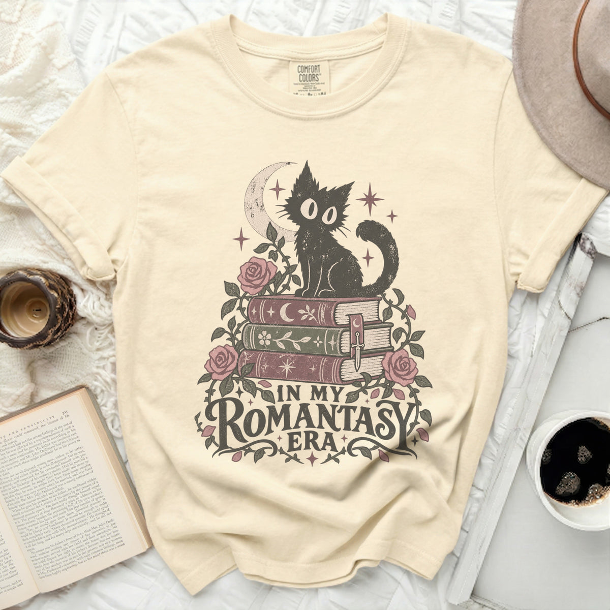 Cream t-shirt with a black cat sitting on books, roses, and moon graphic with text "IN MY ROMANTASY ERA".