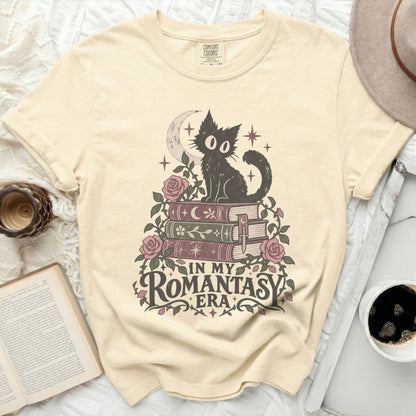 Cream t-shirt with a black cat sitting on books, roses, and moon graphic with text "IN MY ROMANTASY ERA".