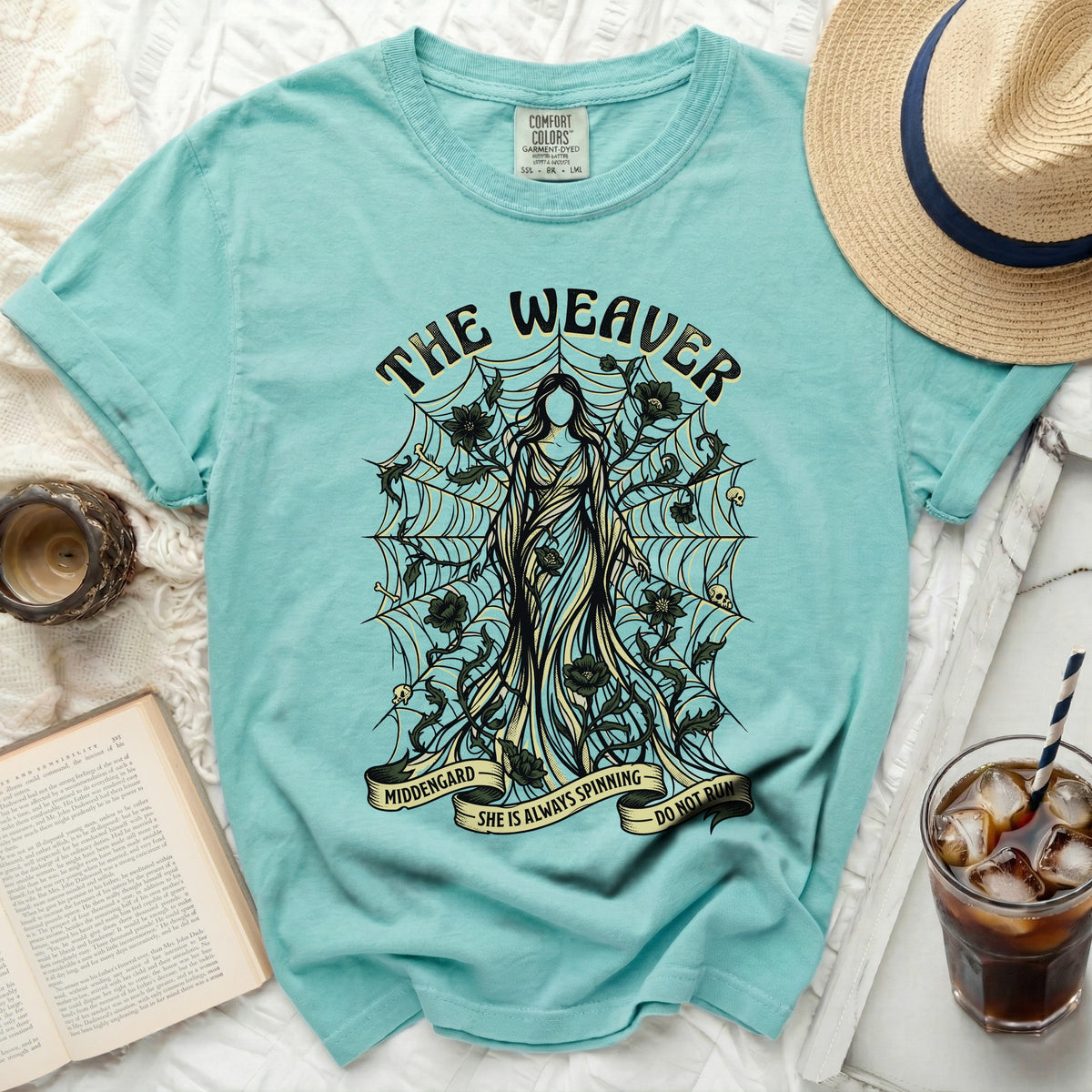 Teal t-shirt with "The Weaver" design of a woman surrounded by webs and skulls.