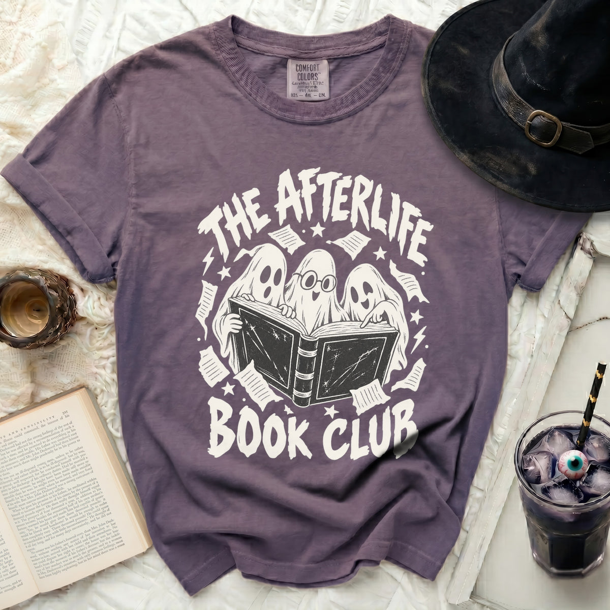Purple t-shirt with white graphic of ghosts reading a book titled "The Afterlife Book Club."