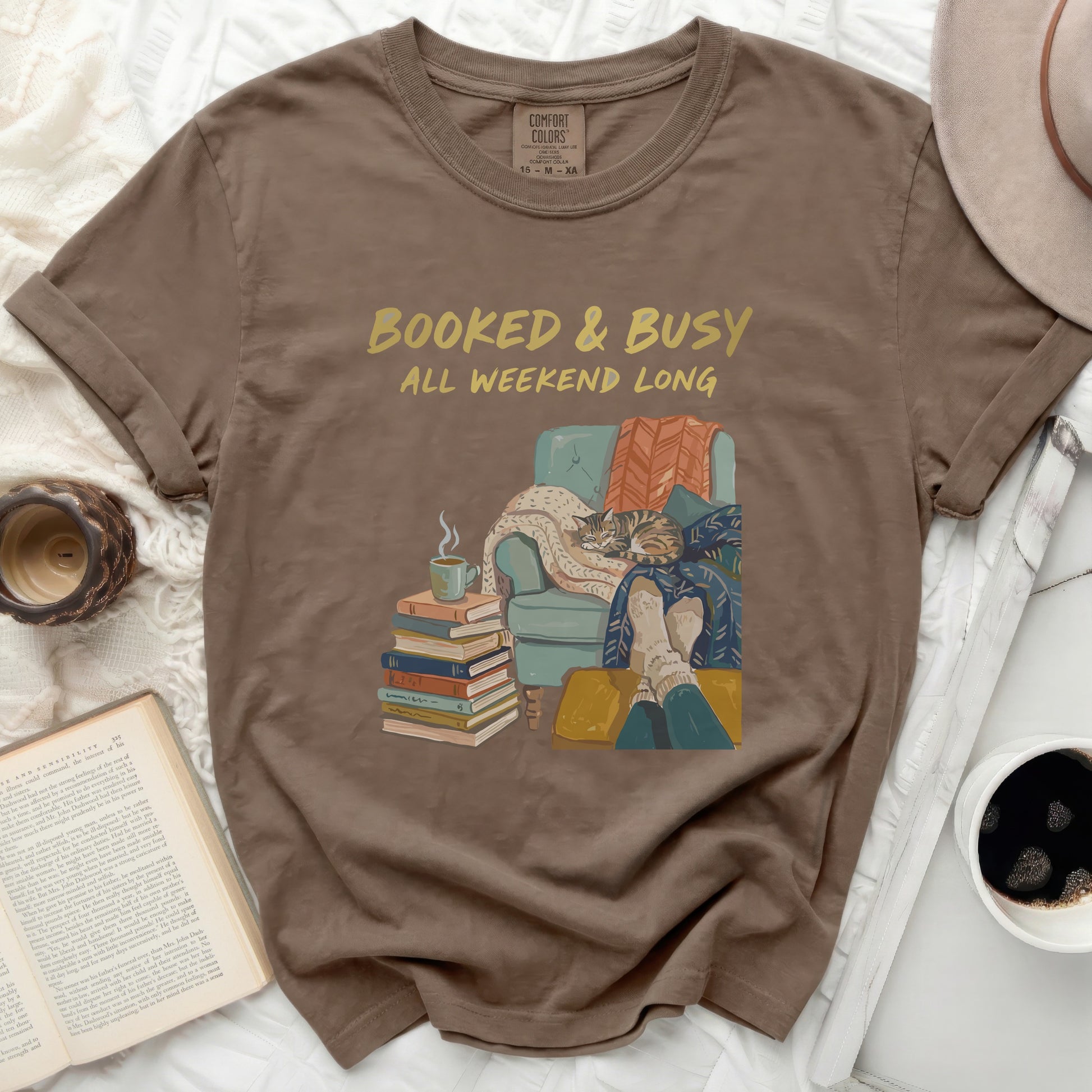 Brown t-shirt with "Booked & Busy All Weekend Long" text and cozy reading illustration.